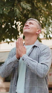 Caucasian mature man tourist praying with closed eyes to God asking for blessing on city town street