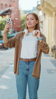 Cheerful Caucasian woman blogger taking selfie on smartphone, talking video call on city street