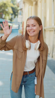 Caucasian woman smiling friendly at camera, hello waving hands gesturing hi, greeting on city street