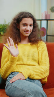 Child kid girl smiling friendly at camera, waving hands gesturing hello hi greeting at home on couch