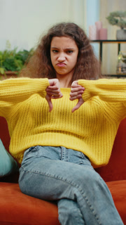 Upset teen girl showing thumbs down, dislike bad work, disapproval, dissatisfied feedback at home