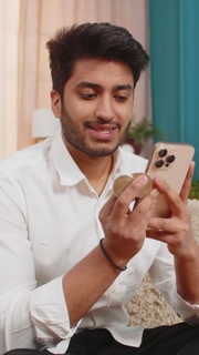 Indian man checking bitcoin wallet balance on smartphone, excited and slightly tense about market