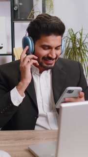 Indian business man working on laptop at home office wearing headphones listening disco music