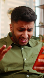 Indian man on home sofa reading bad smartphone news feeling shock stress loss failure problem crisis