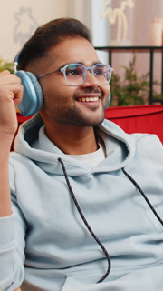 Happy relaxed man in wireless headphones dancing listening favorite disco pop music on home chair