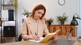 Businesswoman reads leadership book smiles at quotes writes ideas in notebook for growth and vision