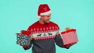 Cheerful man in Santa sweater presenting two Christmas gift boxes, stretches out his hands to camera