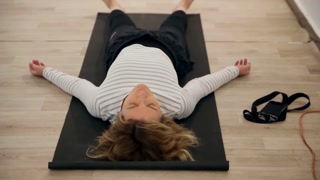Tired woman relaxing after working out. Handheld shot of female resting on yoga mat after exercising in gym. She is in sportswear.