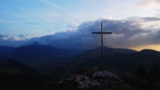 Aerial view of a religious Christian steel cross on a hill in the mountainous countryside, in sunset