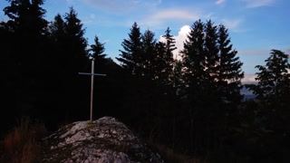 Aerial view of a religious Christian steel cross on a hill in the mountainous countryside, in sunset