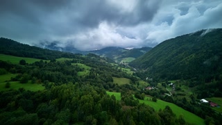Aerial hyperlapse of green valley with forested hills and dramatic cloudy sky before storm