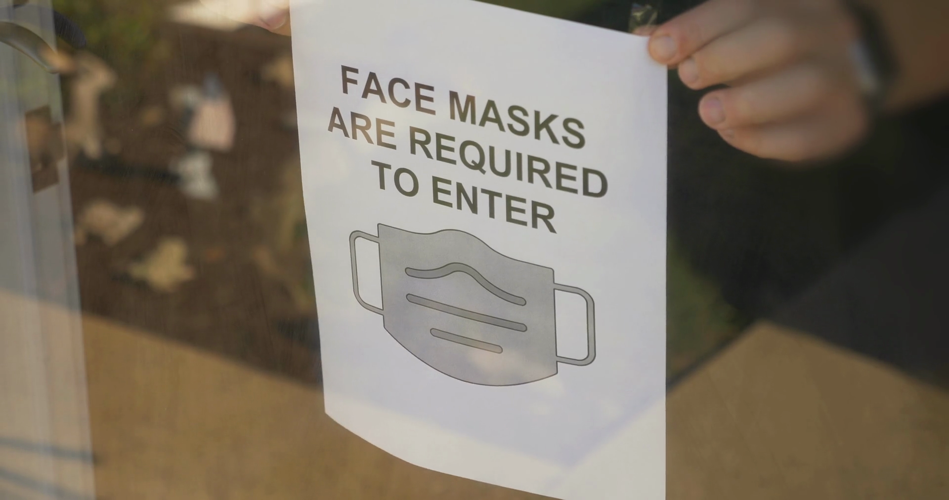 A store owner puts a COVID19 face mask warning sign on the front door