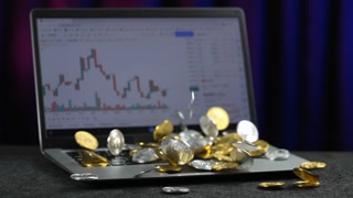 Slow motion view of Bitcoins falling on a laptop showing a wick-and-candle market view screen.