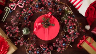 Present box in christmas wreath top view. Hands putting red gift on table close-up. New year and winter time. Holidays and celebration concept. Making surprise.