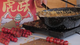 Making fruits in boiling caramel close-up. Chinese winter sweet dessert Tanghulu street food. Berries, tangerine and others fruit caramelized