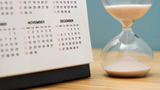 Close up of a calendar and hourglass on wooden table. Concept of starting of new year.