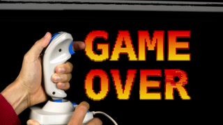 game over text and retro computer arcade with hand holding a joystick in the foreground