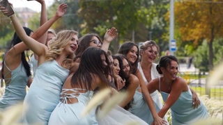Bridesmaids celebrate with bride in park on wedding day.