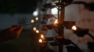Soft glow of oil lamps flickers in Buddhist temple at Vesak. Hand lights lamp, peaceful night scene reflects devotion, reverence. Sacred