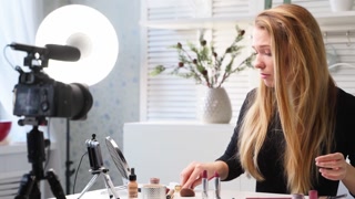 Beauty blogger woman filming makeup tutorial on camera, watching live stream on smartphone. Influencer girl shoots cosmetics product review. Vlogger female shows eye shadow palette, lipstick, mascara
