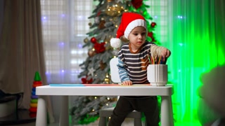 Cute Caucasian baby boy in Santa cap stands at the desk.