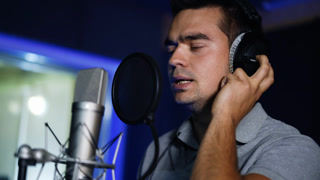 Emotional song performance in modern studio. Male singer wearing headphones sings in a professional microphone. Close up.