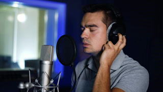 Emotional song performance in modern studio. Male singer wearing headphones sings in a professional microphone. Close up.