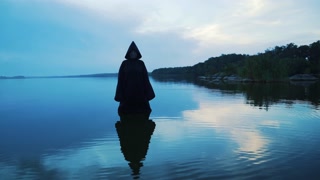 Evil witch in black cloak with hood in the river. Halloween costume.