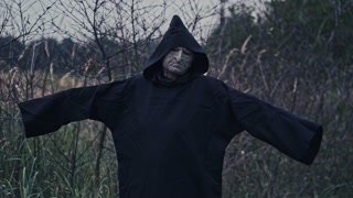 Horror figure in dark costume with hood. Portrait of scary ghost with outstratched arms on nature background. Halloween concept. Vertical video
