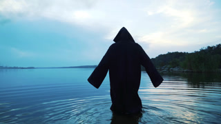 Horror woman soaking in water river. Scary figure in black mantle..  Horror woman soaking in water river. Scary figure in black mantle..