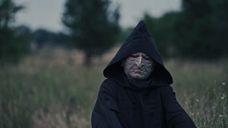 Scary Halloween costume. Portrait of frightful ghost on blur nature background in the evening. Black death in mantle outdoors. Close-up.