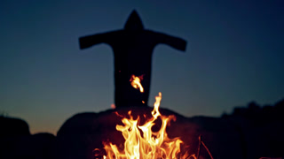 Scary Silhouette of Black Figure on the Hill Behind Fire Orange Flame at Night and Horrorful Death in Cloak with Hood is Waving Arms Halloween Concept