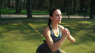 Woman Doing Squats with Resistance Band Outdoors This clip features a young adult woman with dark hair exercising outdoors. She is wearing athletic attire and using a yellow resistance band around her thighs while performing squats on a track and