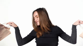 Woman Posing with Shopping Bags on White Background A young adult woman with wavy brown hair and wearing a black long-sleeved top smiles and holds up shopping bags on a white background. She shakes the bags and playfully tosses them at the camera