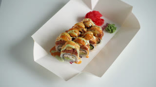Delicious sushi rolls with sauce and tobiko in a takeout box isolated on a white background, concept of japanese food delivery