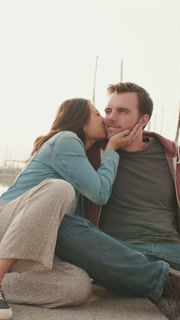 VERTICAL VIDEO: Loving couple kissing while sitting on the embankment
