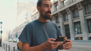 Bearded man strolls down street with cellphone