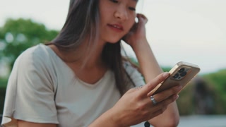 Close up, young woman sits on bench in city park, uses mobile phone