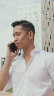 VERTICAL VIDEO: Young businessman talking on smartphone on modern buildings background