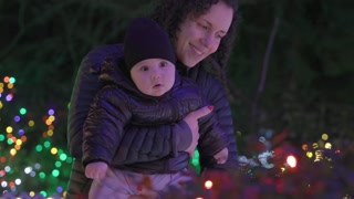 Mother Holding Cute Baby Boy Looking at Christmas Lights. Curious, Observing. Christmastime. Winter, Holidays. Holiday Season.