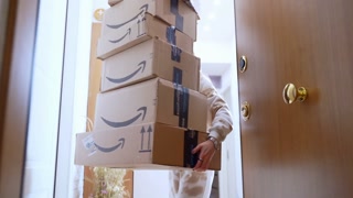 ROME, ITALY - MARCH 15, 2024: Stack of amazon prime cardboards on the doorstep, woman opening the door and picking up her online order