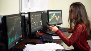 Company worker on the background of monitors in office. World financial trading. Woman calling and checking data of stock market. Shot in 4K (UHD).