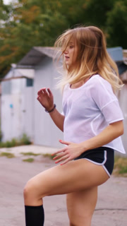 Side view of Athletic young blond woman in white top and shorts exercises leg muscles, jumping Outdoors  in summer. slow motion