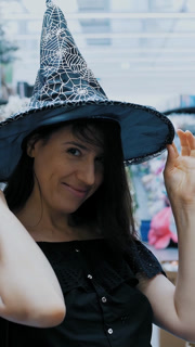 Halloween witch. Halloween party. witch costume. shopping Halloween accessories. in the store, a beautiful brunette woman is trying on a black witch hat for a Halloween party.