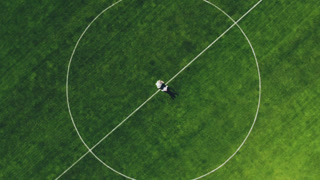 Newlyweds dancing and spinning in center of green football stadium field. Aerial top view of couple celebrating marriage on sports ground.