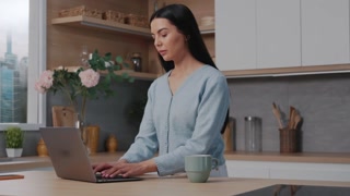 Young beautiful woman using a laptop computer standing serious in the kitchen. Working on notebook at home. Modern apartment. Slow motion