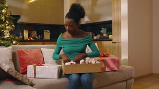 Portrait African American beautiful young woman sitting on sofa hold and preparing Christmas gift box in decorated room. New Year. Holiday