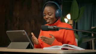 Energetic moving around tracking shot of joyful African American smiling radio host sitting at microphone and talking to radio listeners