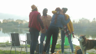 Companions embrace by tranquil water at dawn, Group of friends as morning light reflects on peaceful lake