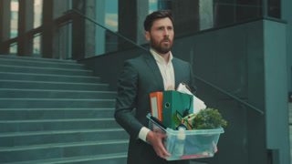 Office worker leaving, Staff member with storage box walking away through empty corporate space with somber attitude